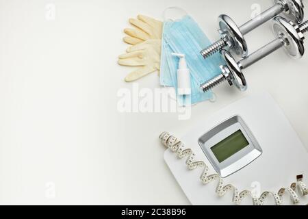 Attrezzature sportive, bilance, maschere mediche e igienizzatore su sfondo bianco. Vista dall'alto, spazio di copia. Fitness. Periodo di isolamento. Peso e controllo della salute Foto Stock
