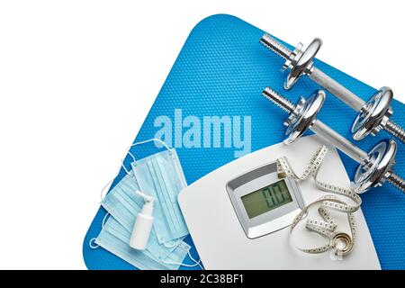 Attrezzature sportive, bilance, maschere mediche e igienizzatore su sfondo bianco. Vista dall'alto, spazio di copia. Fitness. Periodo di isolamento. Peso e controllo della salute Foto Stock