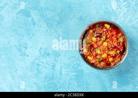 Chili con carne, un stufato messicano con fagioli, carne di manzo macinata, mais e peperoncini, sparato dall'alto su uno sfondo blu w Foto Stock