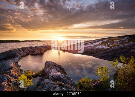 Silhouette di un fotografo con un treppiede in piedi sulle rocce dell'isola al tramonto Foto Stock