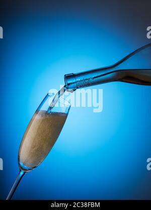 Versare lo champagne da una bottiglia in un bicchiere su sfondo blu Foto Stock