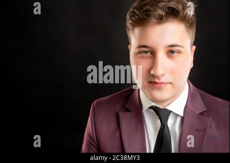 Primo piano ritratto di studente di legge con capelli biondi vestiti con giacca borgogna, camicia bianca e cravatta nera che posa su sfondo isolato con spazio copia A. Foto Stock