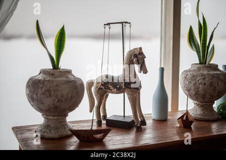 Decorativo cavallo di legno si trova sul tavolo vicino alla finestra fiori in pentole, bottiglia bianca, barca di ferro, elementi di decorazione della stanza, arredamento, Provenza, toni delicati Foto Stock