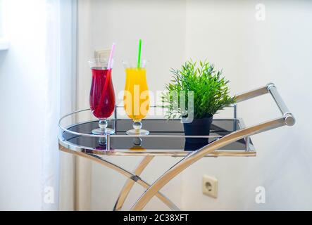 Primo piano di un paio di bevande e fiori decorativi su un carrello di servizio in interni moderni. Cocktail deliziosi. Foto Stock