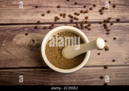 Allspice in un mortaio di ceramica e allspice sparso su un tavolo di legno. Primo piano Foto Stock