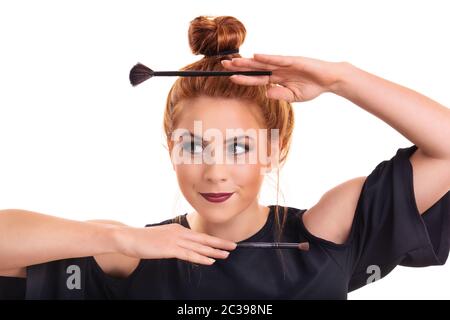 Bella ragazza giovane con pelle perfetta incorniciando il suo viso con spazzole cosmetiche per trucco, sorridente e guardando al lato, isolato su sfondo bianco Foto Stock