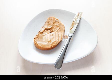 sopra il pane tostato con burro di arachidi cremoso e coltello sul piatto sul tavolo Foto Stock