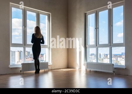 Una ragazza guarda in grandi vetrate in un appartamento vuoto Foto Stock