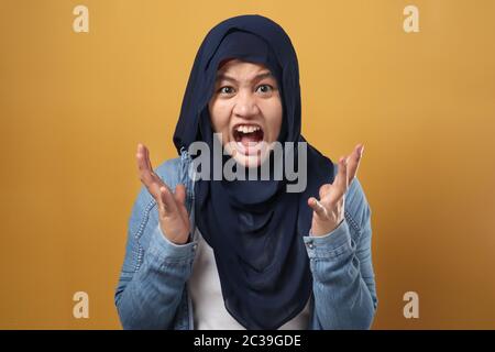 Arrabbiato musulmano ragazza in hijab urlando forte, primo piano ritratto su sfondo giallo Foto Stock