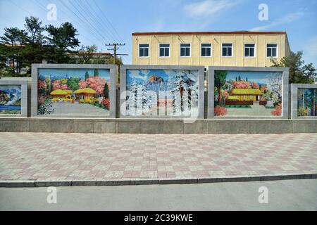 Kaesong, Corea del Nord - 5 maggio 2019: Via in città. Recinzione in cemento con mosaici colorati che raffigurano viste del paese Foto Stock