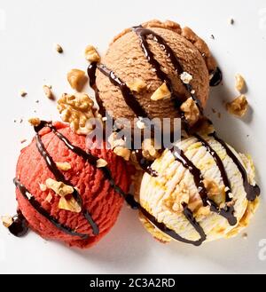 Tre palline di gelato spruzzata con salsa di cioccolato e noci tritate con la vaniglia, cioccolato e frutti di bosco dolce aromatizzato Foto Stock