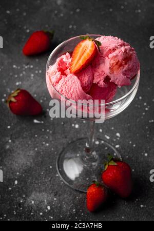 palle di gelato alla fragola con fragole, in un vetro ad alta trasparenza su sfondo scuro Foto Stock