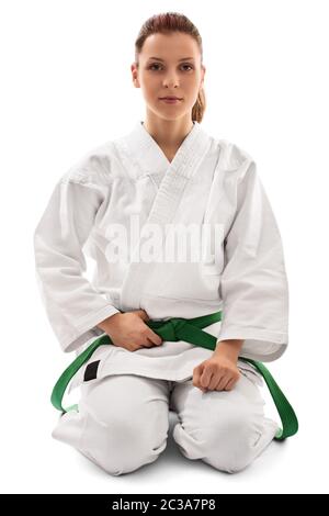 Ritratto di una bella combattente femminile di arti marziali in un kimono bianco con cintura verde in posizione seiza, isolato su sfondo bianco. Calma giovane Foto Stock