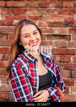 Ritratto di giovane donna in maglia a scacchi in piedi contro un muro di mattoni Foto Stock