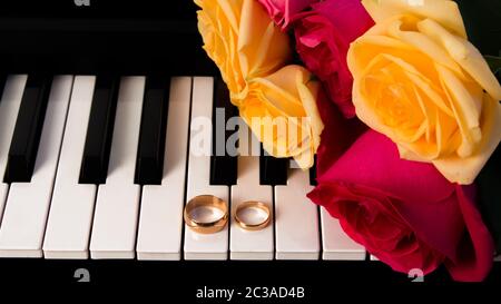 Mazzo di rose giacente sul piano con gli anelli di nozze. Giallo e rose rosse regalo di nozze con le fedi. Preparazione per un matrimonio o di San Valentino d Foto Stock