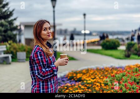 Caffè sul andare. Bella giovane donna azienda tazza da caffè e sorridente nel parco Foto Stock