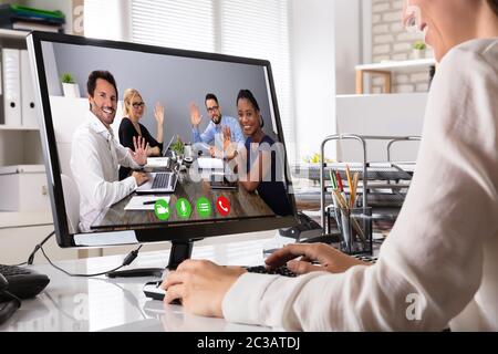 Giovane donna d'affari in videoconferenza con i colleghi saluto Lei sul computer portatile in ufficio Foto Stock