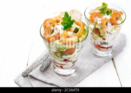 Pasta con insalata di gamberetti, avocado, Fresco cetriolo e peperone e pomodoro condito con salsa di yogurt in due bicchieri di vetro su un tovagliolo, pane e delle forcelle Foto Stock