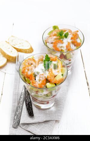 Pasta con insalata di gamberetti, avocado, Fresco cetriolo e peperone e pomodoro condito con salsa di yogurt in due bicchieri di vetro su un asciugamano, pane e delle forcelle Foto Stock