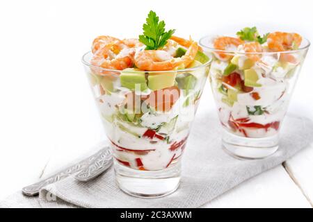 Pasta con insalata di gamberetti, avocado, Fresco cetriolo e peperone e pomodoro condito con salsa di yogurt in due bicchieri di vetro su un tovagliolo, pane e delle forcelle Foto Stock