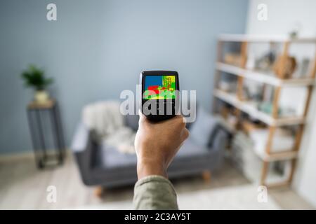 Donna di mano utilizzando termocamera infrarossa per controllare la temperatura nel soggiorno Foto Stock