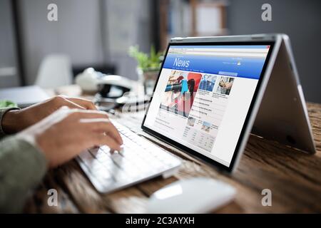 Immagine ritagliata di imprenditore per leggere le notizie sul portatile in ufficio Foto Stock