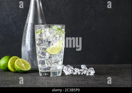 Bicchiere di acqua frizzante con cubetti di ghiaccio e fetta di calce Foto Stock