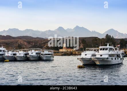 Barche in piedi lungo la riva del mare rosso contro lo sfondo delle montagne e il cielo blu Foto Stock