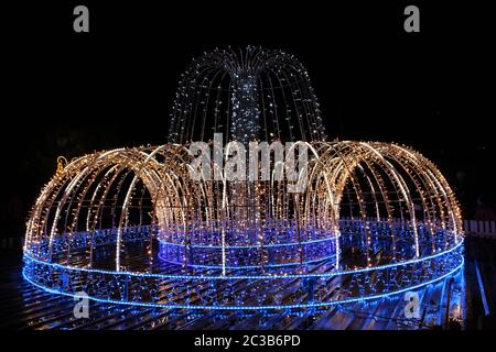 Bella fontana di colorati ghirlande vacanza scintillante e lampeggiante nel parco della città in inverno Foto Stock