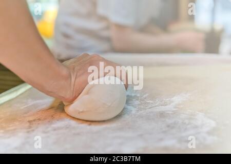Persona mano che rotola fuori l'impasto fatto da farina, che sarà usato per la fabbricazione di gnocchi cinesi tradizionali durante la lezione di cottura in un viaggio Foto Stock