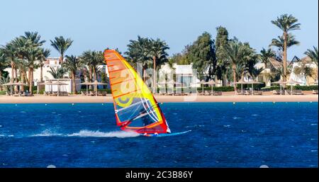 Windsurf in acqua blu sullo sfondo della spiaggia con ombrelloni e palme in Egitto Foto Stock