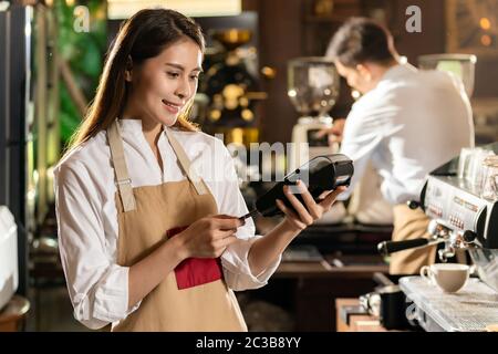 Asian Barista effettuare il pagamento con la carta di credito del cliente utilizzando la tecnologia chip EMV per l'acquisto di caffè in un bar caffetteria. Foto Stock