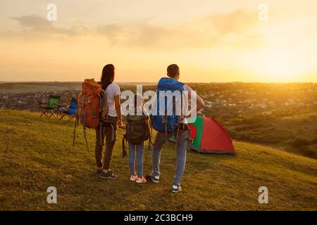 Famiglie con bambini turisti con zaini ammirando il tramonto in un campeggio avventura in natura Foto Stock