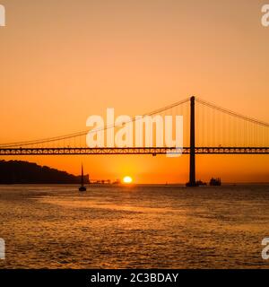 Tramonto scenario con la sagoma della barca a vela che va in direzione del 25 aprile ponte con il sole sopra l'orizzonte. Foto Stock