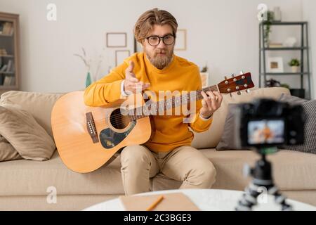 Giovane insegnante di musica che spiega qualcosa o risponde alla domanda del pubblico online durante la lezione in ambiente domestico Foto Stock