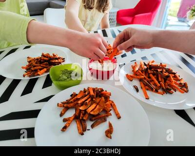 Foto delle mani di famiglia che raggiungono patatine fritte, guacamole e salsa bianca Foto Stock