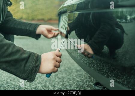 Una persona che ruba la targa su una macchina parcheggiata con un cacciavite Foto Stock