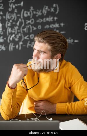Insegnante con portatore di penza in pullover giallo pensando a una nuova lezione di fronte al laptop, mentre si ha una breve pausa tra le lezioni online Foto Stock
