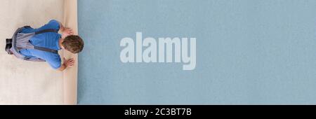 Angolo di Alta Vista del lavoratore in uniforme svolgimento tappeto sul pavimento Foto Stock