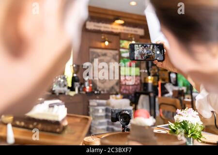 Vista posteriore di due blogger di adulti giovani asiatici imprenditore proprietario review caffetteria Cafe per i social media e il marketing online in cafe. Utilizzando per sta Foto Stock