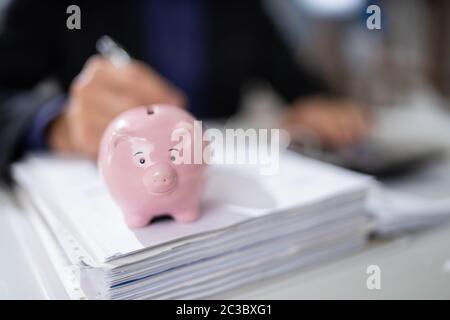 I mediatori controllo fattura con Rosa Piggybank sulla scrivania Foto Stock