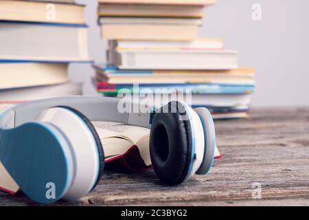 libro con le cuffie davanti a mucchi di libri diversi su tavolo di legno Foto Stock