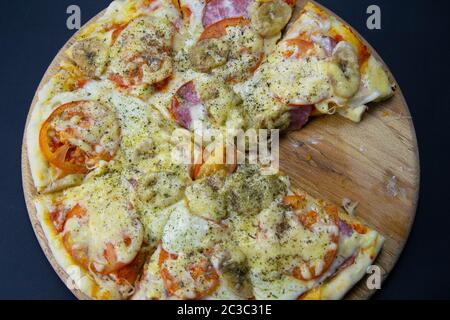 Pizza con mozzarella di bufala, salame, pomodori e banane senza un singolo pezzo, sorge su una tavola di legno su uno sfondo nero. viste dall'alto Foto Stock