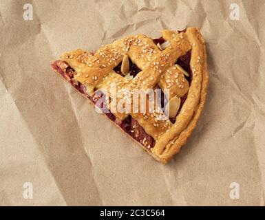 Sezione triangolare di cotto ciliegia sulla torta di carta marrone, vista dall'alto, blu sullo sfondo di legno Foto Stock