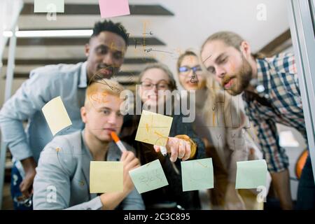 Business, startup, pianificazione e concetto di persone. Team multietnico creativo e felice con colleghi disabili in sedia a rotelle che guardano le carte in ufficio Foto Stock