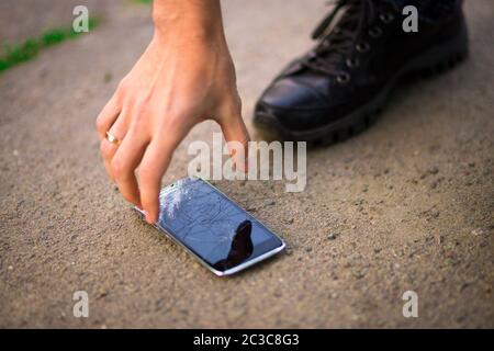 Persona che sceglie lo smartphone rotto schermo rotto a terra Foto Stock