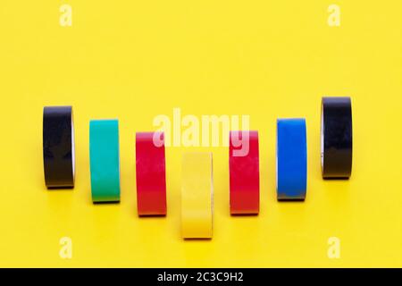 Nastri elettrici isolati. Primo piano di una serie di rotoli colorati di nastri adesivi isolanti su sfondo giallo. Fotografia macro. Foto Stock