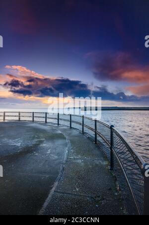 Un'alba d'inverno sul molo di Tynemouth, che guarda fuori sopra le ringhiere attraverso il porto sul mare del nord e la luce del sole che sorge sulle nuvole Foto Stock