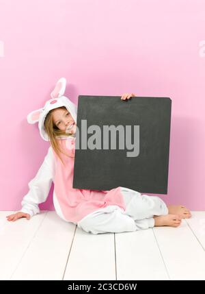 bella ragazza bionda con intimo costume di coniglio e lavagna si posa in studio ed è felice Foto Stock