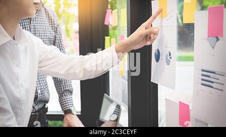Uomo d'affari di incollaggio note adesive sulla parete di vetro in ufficio e discussting con il team. Foto Stock